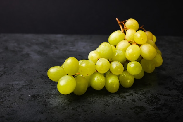 Foto de uva verde sobre un fondo oscuro de mármol. Uvas volumétricas. Un racimo de arbusto de uva verde.