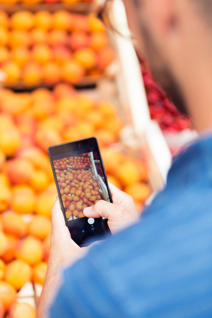 Foto foto de vendedor haciendo una foto con su teléfono inteligente a las naranjas en la tienda de abarrotes de salud.