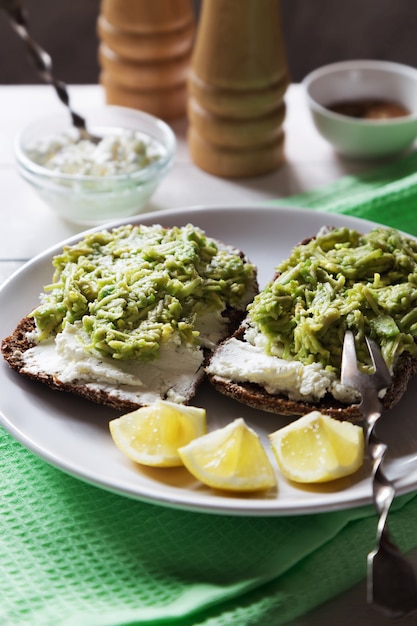 Foto foto vertical de bocadillos de aguacate con requesón y rodajas de limón.