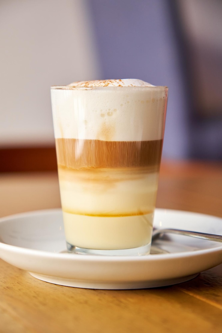 Foto foto vertical de un café con leche servido en un vaso de cristal en la parte superior de un plato de porcelana en una superficie de madera