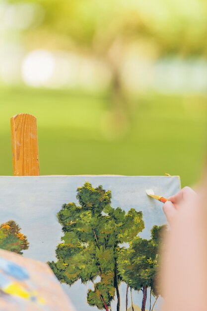 Foto vertical com foco seletivo na pintura à mão de uma mulher com um pincel em uma tela