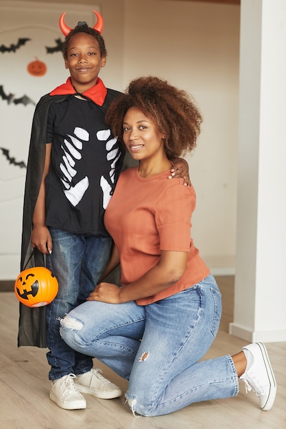 Foto vertical completa de uma mulher bonita e seu filho pré-adolescente usando uma fantasia de diabinho no Halloween