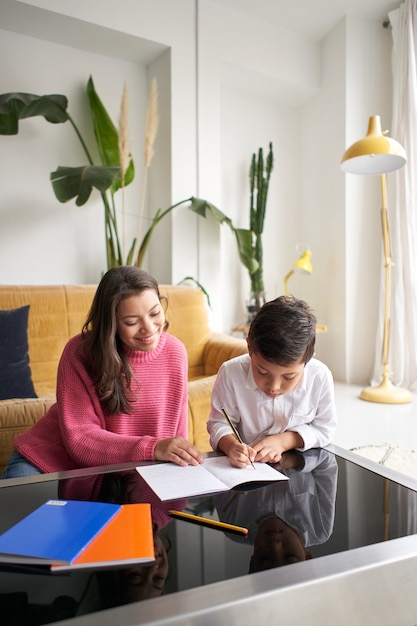 Foto vertical da mãe ajudando o filho com o dever de casa na sala de estar de casa