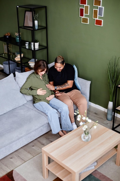 Foto vertical de alto ângulo de um casal gay moderno com uma jovem grávida olhando fotos de bebê
