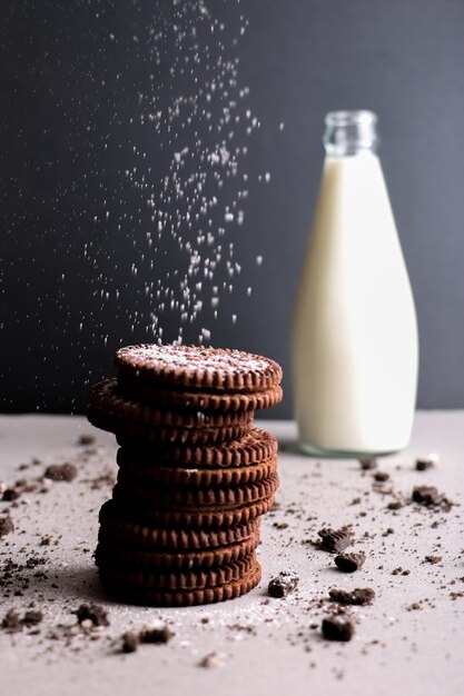 Foto vertical de biscoitos de cacau empilhados uns sobre os outros e uma garrafa de leite polvilhada com farinha