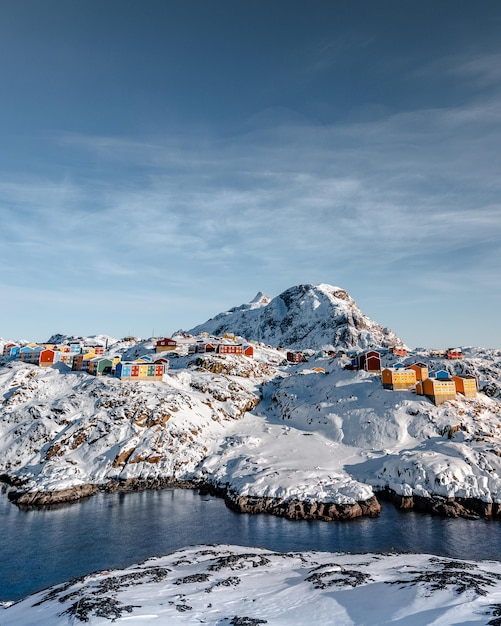 Foto vertical de casas coloridas nas montanhas nevadas perto de um rio congelado na Groenlândia