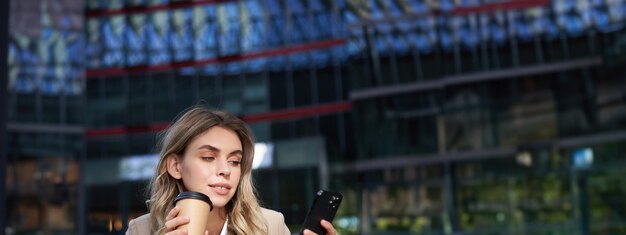 Foto foto vertical de empresária bebe café e olha para mulher corporativa de aplicativo de celular em seu almoço