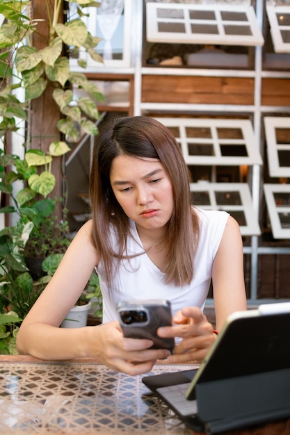 Foto vertical de mulher asiática navegando nas mídias sociais em celular sentindo-se triste e deprimida