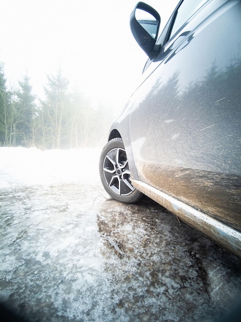 Foto vertical de um carro elétrico estacionado em uma poça congelada no inverno com uma paisagem branca na frente