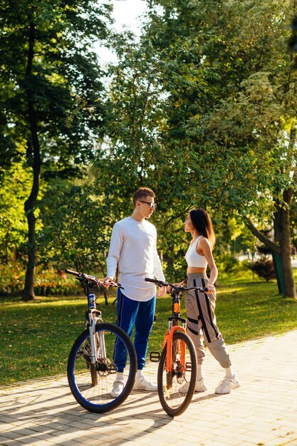 Foto vertical de um casal alegre de ciclistas conversando no parque