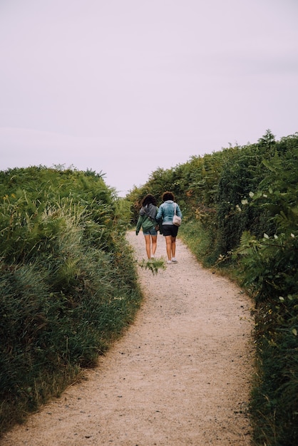 Foto vertical de um casal de lésbicas caminhando em um caminho cercado por vegetação