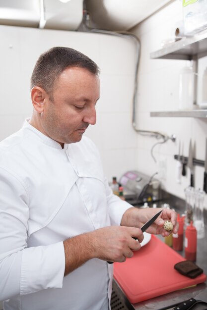 Foto vertical de um chef profissional abrindo ovo de codorna com uma faca