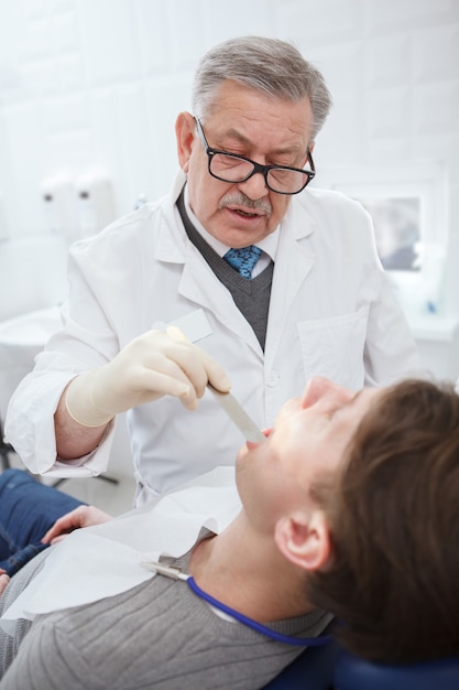Foto vertical de um dentista profissional falando com o paciente enquanto examina seus dentes
