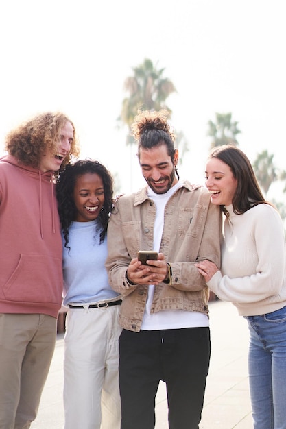 Foto foto vertical de um grupo de amigos felizes usando o telefone ao ar livre enquanto caminham rindo