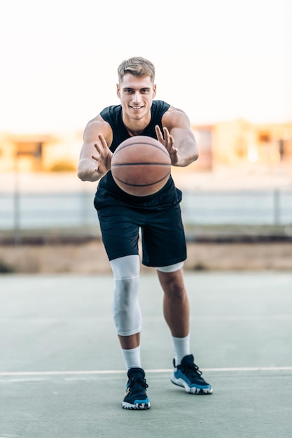 Foto vertical de um jogador de basquete passando a bola em uma quadra ao ar livre