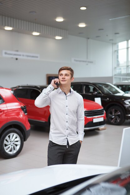 Foto foto vertical de um jovem feliz falando ao telefone na concessionária de automóveis