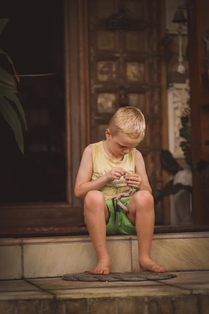 Foto vertical de um menino branco branco brincando com uma cobra