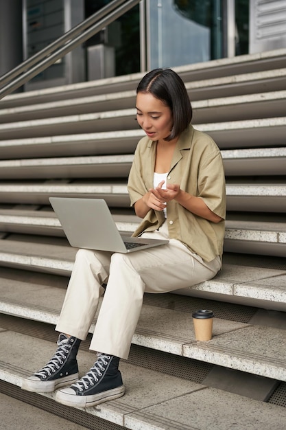 Foto vertical de uma estudante asiática participando de uma reunião on-line conversando no chat de vídeo do laptop sentado