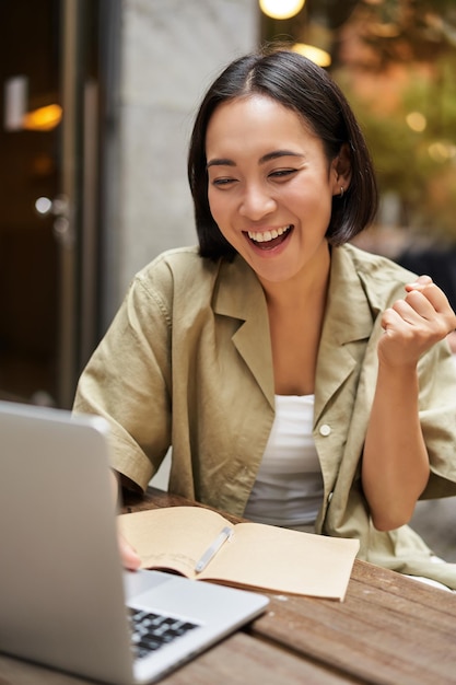 Foto vertical de uma garota feliz falando em videochamada olhando para um laptop em uma reunião on-line sentada