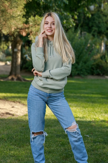 Foto vertical de uma jovem parada no parque e sorrindo para a câmera