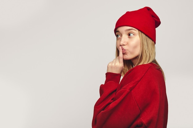 Foto vertical de uma linda garota hipster beijando o dedo indicador parece misteriosamente