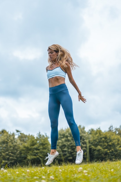 Foto vertical de uma modelo feminina esticando o corpo pulando no jardim