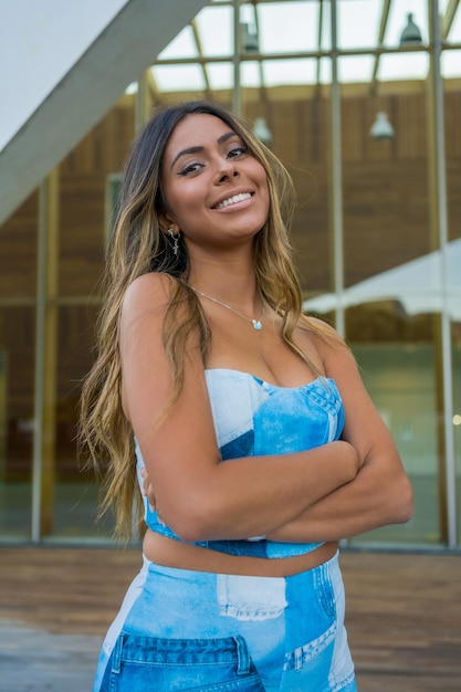 Foto vertical de uma mulher bonita em roupas de ganga de pé com o braço cruzado sorrindo para a câmera