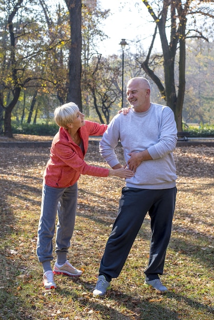 Foto vertical de uma mulher caucasiana sênior ajudando o marido enquanto corria em um parque juntos