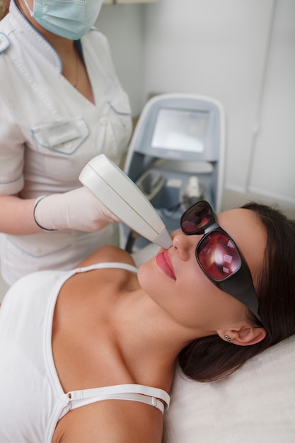 Foto vertical de uma mulher fazendo depilação a laser do lábio superior na clínica de cosmetologia