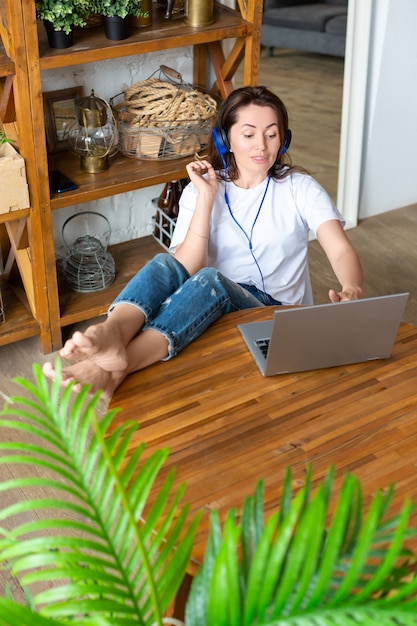 Foto vertical de uma mulher feliz e sorridente em fones de ouvido azuis na frente de um monitor de laptop em casa ...