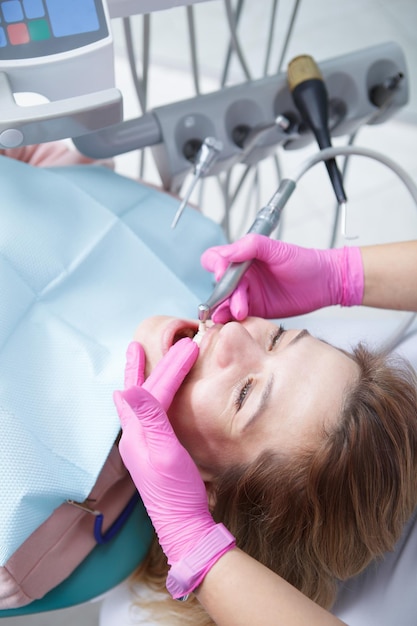 Foto vertical de uma mulher madura fazendo limpeza dentária profissional no consultório do dentista