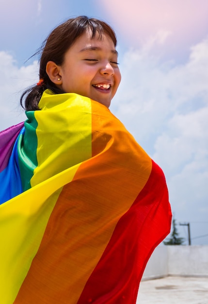 Foto vertical de uma pequena menina sorridente com uma bandeira de arco-íris