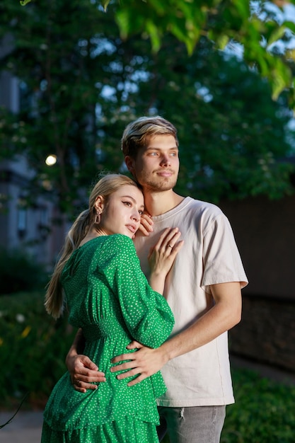 Foto vertical do jovem casal se abraçando e olhando de lado na rua à noite