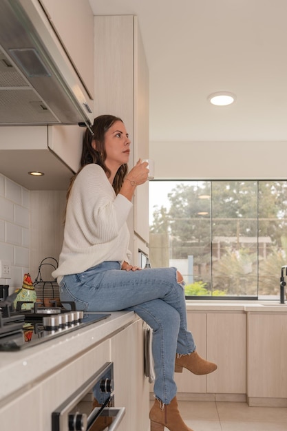 Foto vertical do perfil de uma mulher tomando café em uma cozinha nova