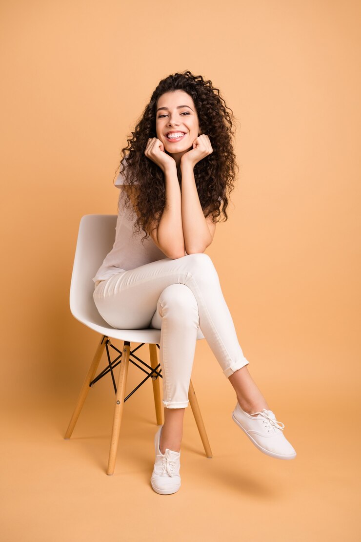 Foto vertical em tamanho real de uma senhora incrível sentada em uma cadeira confortável bom humor inspirado para começar o dia de trabalho usar roupas casuais isoladas de fundo bege