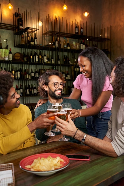 Foto vertical de un grupo de compañeros de trabajo brindando con cerveza en el bar del restaurante después del trabajo en el pub happy hour