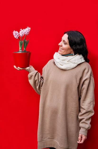 Una foto vertical de una hermosa mujer sosteniendo una maceta con plantas de jacinto en la pared roja