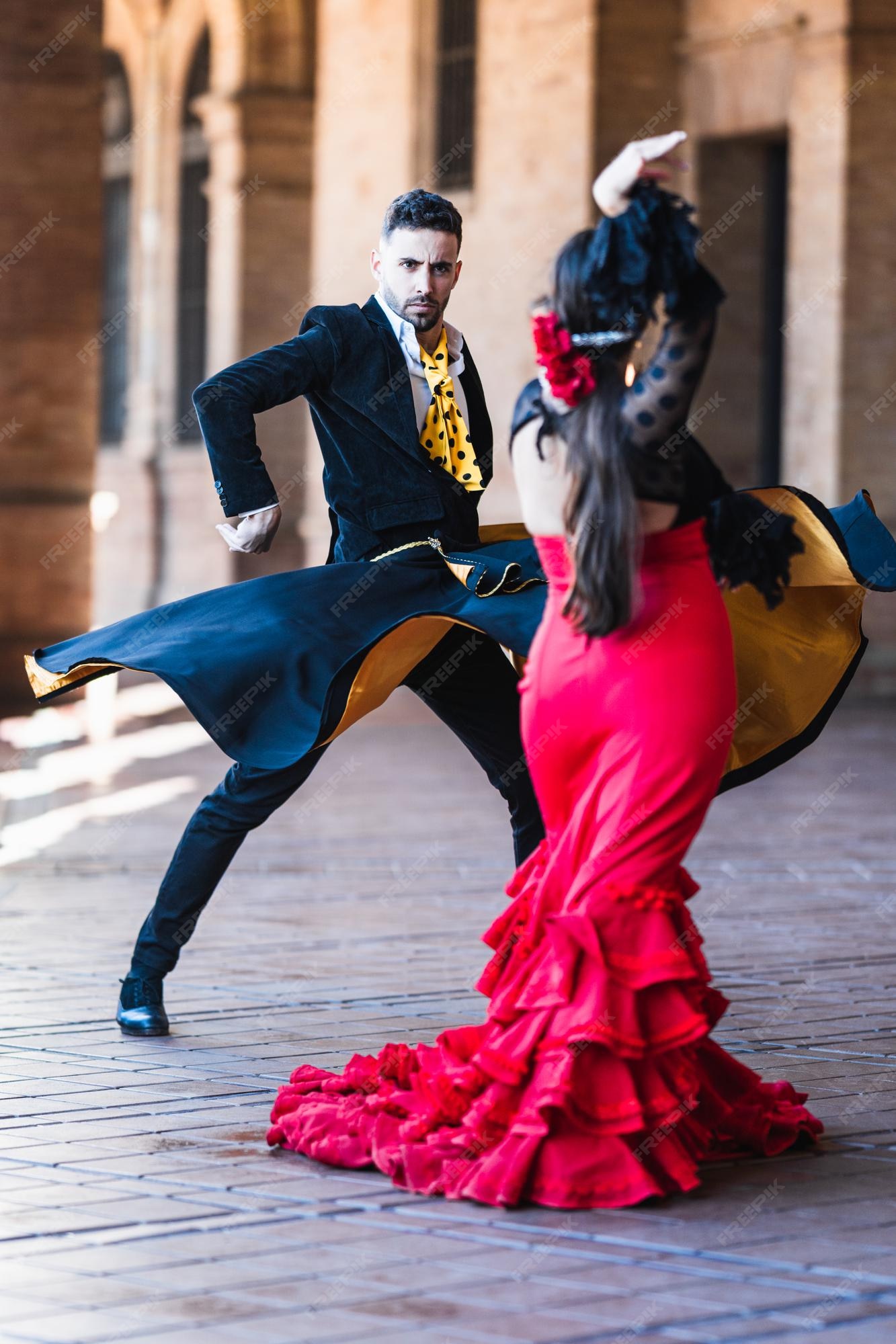 Foto vertical de un hombre con una capa bailando flamenco con mujer en traje de flamenca al aire libre | Foto Premium