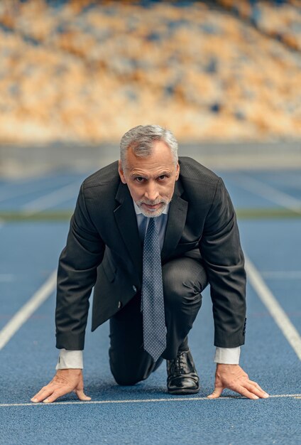 Foto foto vertical de un hombre vestido con traje de negocios y corbata mirando a la cámara mientras se paraba al comienzo de la pista de carreras preparándose para correr