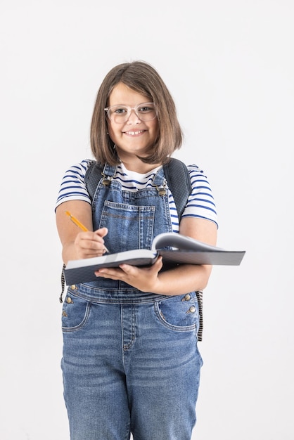 Foto vertical de una joven con anteojos tomando notas en un libro de ejercicios mientras está de pie