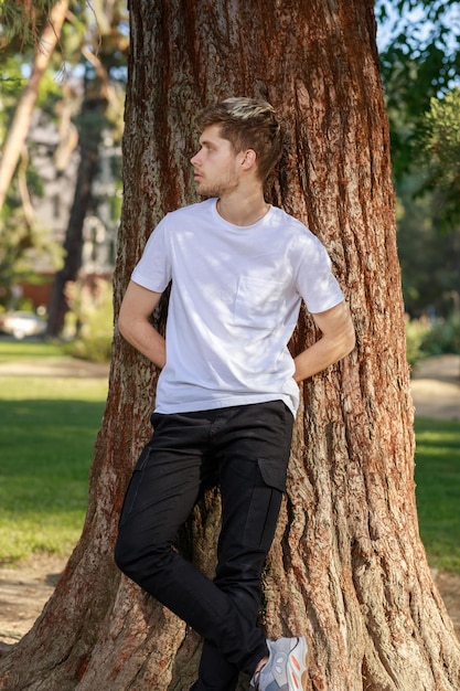 Foto vertical de un joven apoyado en el árbol del parque