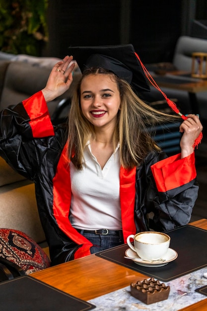 Foto vertical de una joven con capa de graduación y una cámara sonriente en el restaurante