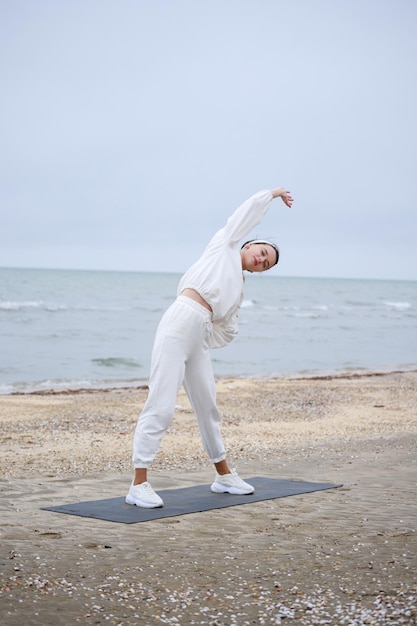 Foto vertical de una joven parada en la colchoneta de yoga y estirando su cuerpo Foto de alta calidad