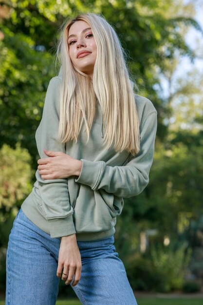 Foto vertical de una joven parada en el parque y mirando a la cámara