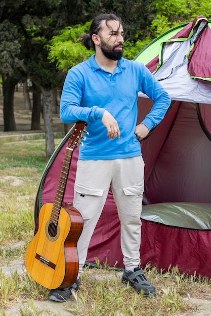 Foto vertical de un joven sosteniendo una guitarra y parado frente a la carpa