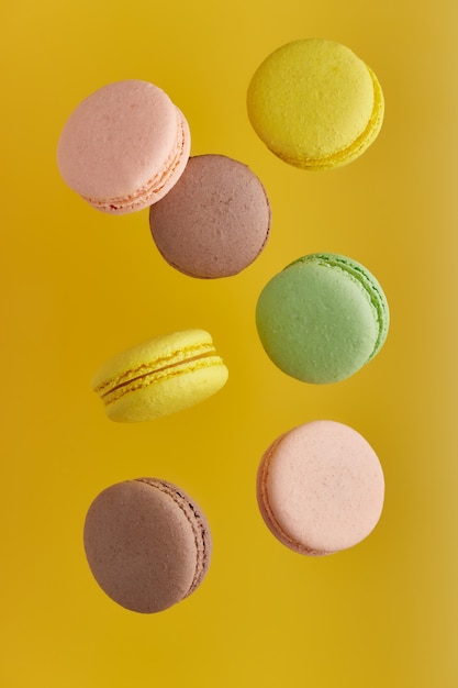 Foto vertical de macarrones. Macarrón de pastel colorido con tonos pastel en levitación caótica sobre superficie amarilla Vista superior de galletas de almendra.