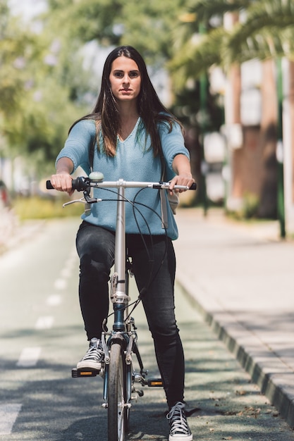 Foto vertical de una mujer joven con una bicicleta en la calle