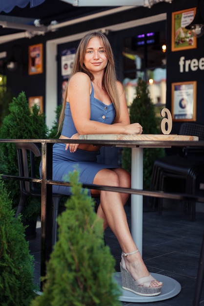 Foto vertical de una niña en un café. Una chica con una blusa azul se sienta de lado.