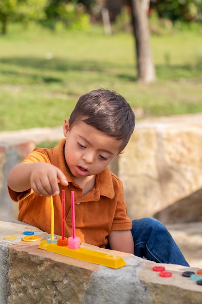 Foto vertical de un niño con discapacidad intelectual aprendiendo con juguetes educativos en un parque natural