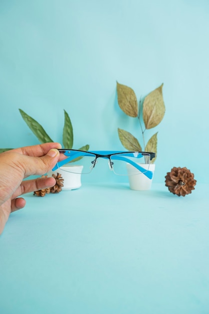 Foto vertical. óculos, mãos, flores de pinheiro e folhas verdes em fundo de papel rosa. ideia de conceito minimalista